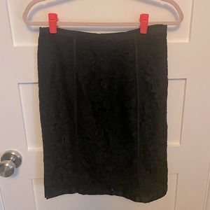 Black lace pencil skirt. Lined, with small side slit and trimmed ribbon detail.